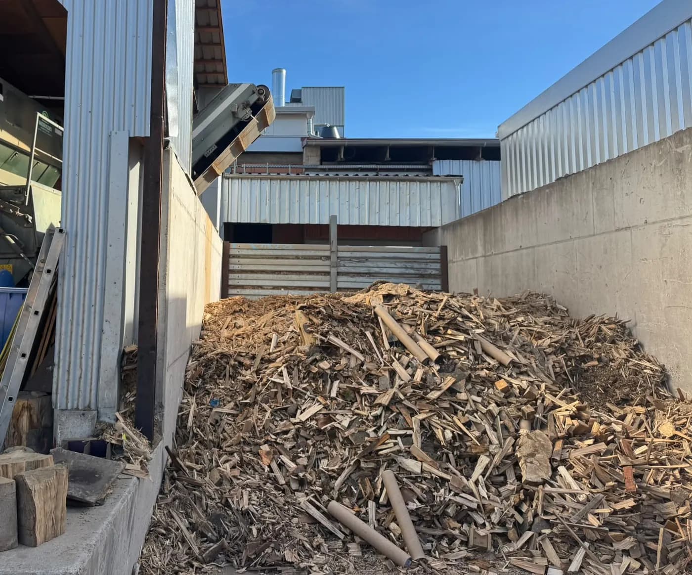 Haufen aus Rinde und Holzresten neben der Halle des Brennholzwerks